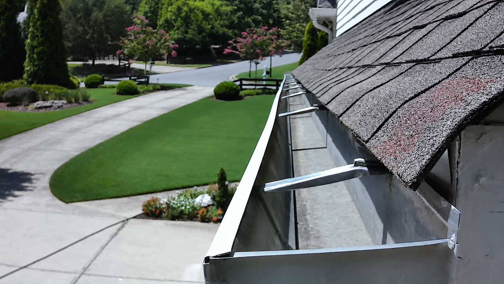 Freshly cleaned white aluminum gutter along a shingled roof edge overlooking a manicured lawn